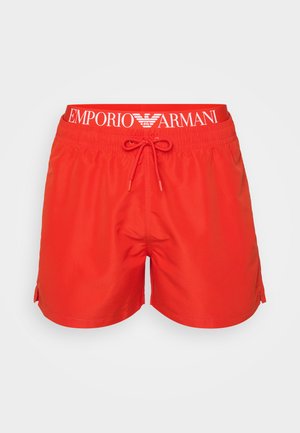 Červené plavkové šortky vyrobené z ľahkého materiálu, s elastickým pásom a bielym logom, a bočnými rozparkami pre väčšiu slobodu pohybu.