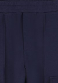 Gros plan sur un tissu bleu foncé avec une ceinture et des détails de couture verticaux, mettant en valeur la texture et les motifs de couture.