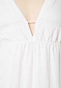 Robe blanche avec un décolleté en V, texture froncée et plis subtils. Fabriquée en tissu léger, avec des détails de couture minimaux.