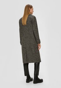 Lange houndstooth-gestreepte jas in zwart en beige, met lange mouwen en een rechte snit, gecombineerd met zwarte leren broeken en enkellaarsjes.