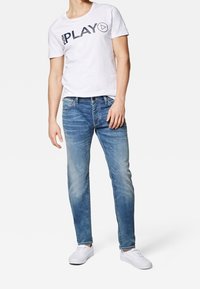 Camiseta de algodón blanca con texto negro "PLAY", jeans azules con acabado desgastado y zapatillas blancas. Conjunto simple y casual.