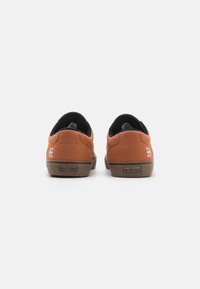 Brown canvas sneakers with black interior, featuring a rubber sole and white Etnies logo on the heel. Classic low-top design.