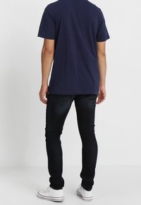 Camiseta de manga corta azul marino combinada con jeans de mezclilla oscuros. La camiseta tiene un cuello redondeado; los jeans tienen un ajuste recto con bolsillos traseros.