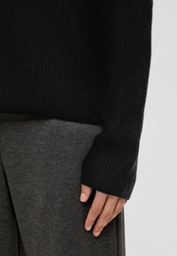 Czarny sweter ribbed o luźnym kroju, z długimi rękawami. Połączony z szarym materiałem, prawdopodobnie spódnicą lub spodniami, o miękkiej fakturze.