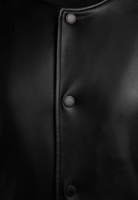 Black leather garment with visible stitching and three round buttons embossed with brand text along the front closure.