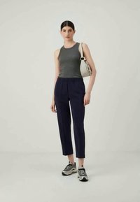 Γκρίζα αμάνικη μπλούζα συνδυασμένη με ναυτικές tapered παντελόνες. Το μοντέλο κρατά μια μικρή λευκή τσάντα και φορά μαύρα και λευκά αθλητικά παπούτσια. Απλός, μοντέρνος σχεδιασμός.