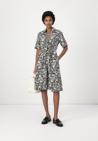 Abito camicia a fantasia floreale in bianco e nero con maniche corte, vita stretto e gonna ampia. Abbinato a mocassini neri e una borsa bianca.