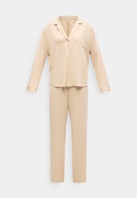 Μπεζ πυτζάμα με κουμπιά, μακριά μανίκια και τσέπη στο στήθος, με παντελόνι σε ίσια γραμμή, σε απλό φόντο.