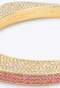 Bransoletka w odcieniu złota o zaokrąglonym kształcie, ozdobiona iryzującymi i różowymi kamieniami rhinestone. Gładka faktura z błyszczącymi metalowymi akcentami.