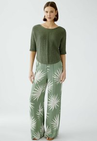 Grüner gestrickter Crop-Top mit Rundhalsausschnitt, kurzen Ärmeln und strukturierter Textur; weit geschnittene, pastellgrüne Hose mit weißen Blättermuster.