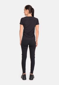 Melna sporta topa un pieguļošas bikses ar sānu svītrām. Materiāls izskatās elastīgs. Modelis stāv ar muguru, valkājot masīvas melnas kedas.