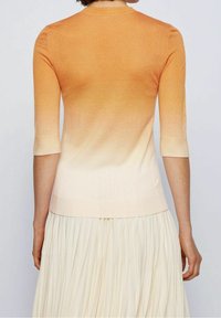 Haut en maille dégradée orange et crème avec manches courtes et encolure ronde, présentant une texture lisse et une silhouette ajustée.