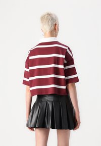 Μαρόνο και άσπρο ριγέ κοντό μπλουζάκι με κλασικό γιακά, συνδυασμένο με μια μαύρη πλισέ μίνι φούστα από ψεύτικο δέρμα.