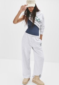 Graue Sweatpants mit Kordelzug, navyblauem Body und grauem Sweatshirt mit grüner "Los Angeles" Schrift. Beiges Knöchelboot vervollständigt das Outfit.