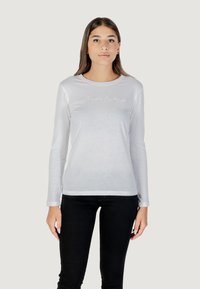 Camicia bianca a maniche lunghe realizzata in materiale leggero, con scollatura tonda e un logo sottile in cucitura testurizzata sul petto.