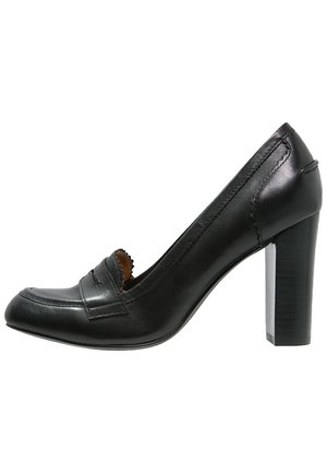 Zwarte leren hoge hak schoen met een afgeronde neus, subtiele stikdetails en een gestructureerde blokhak. Klassiek ontworpen met een loaferaccent.