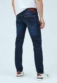 Mörkblå jeans med slim fit, fem fickor, kontrasterande sömmar och en brun läderlapp på baksidan av midjebandet.