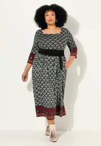 Svart klänning med kort ärm och blommönster, fyrkantig halsringning, vinröda detaljer och svart midjeband. Midilängd med sidofickor.