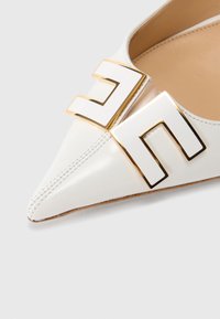 Λευκό δερμάτινο παπούτσι με μυτερή μύτη και επίπεδη σόλα, με χρυσό και λευκό γεωμετρικό διακοσ μητικό στο επάνω μέρος και διακριτικές ραφές κατά μήκος της άκρης.