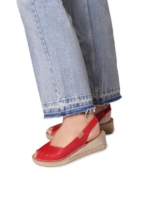 Sandali wedge espadrille rossi in pelle, con punte scoperte, suole avvolte in juta e cinturini alla caviglia, abbinati a jeans con orlo sfilacciato.