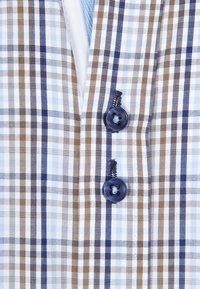 Kostkovaná látka s modrými, hnědými a bílými pruhy; obsahuje dva tmavé knoflíky a texturované šití poblíž knoflíků.