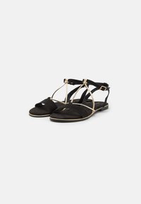 Black suede sandals with crisscross straps, gold accents, and a flat sole. Open back design with ankle strap for secure fit.
