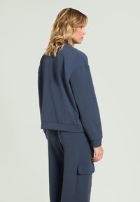 Marineblauwe sweatshirt met een losse pasvorm, geribbelde manchetten en een cropped zoom, gecombineerd met bijpassende broek met een zijladingzak.