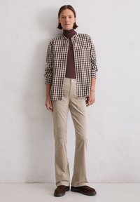 Checkered brown and white button-up shirt layered over a dark brown turtleneck, paired with beige flared pants and dark brown shoes.