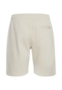 Pantalones cortos de algodón color beige claro con cinturilla elástica, textura suave y un único bolsillo trasero con una pequeña etiqueta.