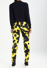 Svart stickad kort tröja som matchas med gula och svarta mönstrade cargo-byxor, som har en glänsande yta och flera fickor.