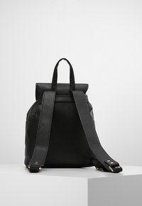 Zaino nero in pelle con design a risvolto, spallacci robusti e texture liscia. I dettagli in metallo dorato aggiungono un tocco di eleganza.
