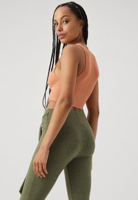 Ribbet, kort tanktopp i fersken, parret med høy livet, olivengrønn leggings. Har en tettsittende design og teksturert stoff.