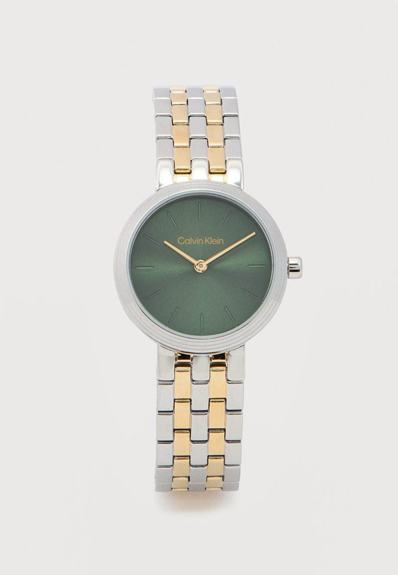 Ρολόι χειρός Calvin Klein με πράσινο καντράν, χρυσά δείκτες, ασημένιο και χρυσό μπρασελέ με συνδέσμους, και μινιμαλιστικούς δείκτες ώρας σε λευκό φόντο.