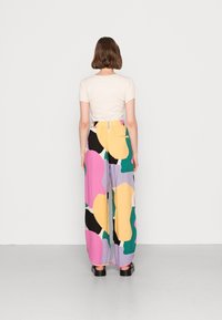 Ensemble en deux pièces comprenant un haut crème ajusté à manches courtes et volantées, et un pantalon à jambes larges avec un motif abstrait multicolore.