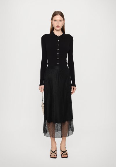 Cardigan preto de manga longa com botões, combinado com uma saia midi em rede preta. O conjunto apresenta camadas transparentes e sandálias de salto pretas com tiras.