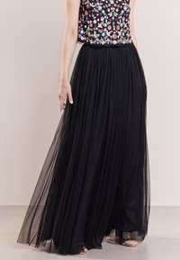 Jupe longue en tulle noir à plusieurs couches, associée à un crop top brodé de motifs floraux colorés sur fond sombre.