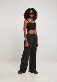 Black cropped tank top and wide-leg black pants, made of soft fabric. The outfit features an elastic waistband and paired with black sandals.