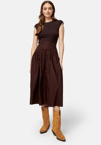 Robe en coton marron avec un corsage ajusté et une jupe froncée, associée à des bottes de cowboy en suède beige avec un bout pointu et des coutures décoratives.