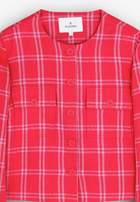 Chaqueta a cuadros rojos con botones, dos bolsillos en el pecho, cuello redondo y cuatro botones. El material parece texturizado y ligero.