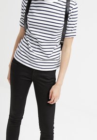 Camiseta de manga corta a rayas en blanco y marino, con un ajuste relajado y un cuello redondo, combinada con unos vaqueros negros ajustados y una correa negra.