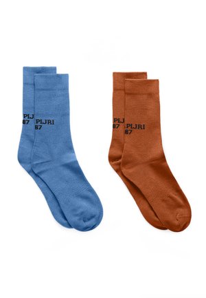 Dwie pary skarpetek za kostkę, jedna niebieska, a druga rdzawo-pomarańczowa, każda z czarnym napisem "PJ RJ 87" w pobliżu kostki.