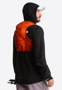 Czarna wodoodporna kurtka o dopasowanym kroju, z pomarańczową kamizelką nawadniającą na plecach, regulowanymi paskami i odblaskowymi elementami.