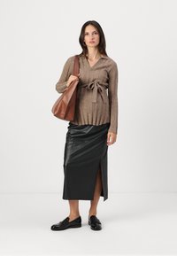 Pull en maille brun avec ceinture à nouer, associé à une jupe midi en cuir noire avec fente latérale, et des mocassins noirs. Sac à main brun.