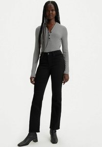 Jeans acampanados negros combinados con una blusa de rayas en blanco y negro de manga larga, que cuenta con un escote abotonado y una silueta ajustada.