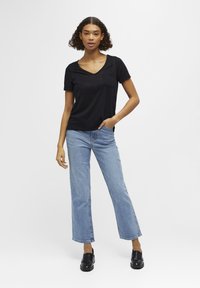 Zwart T-shirt met korte mouwen en V-hals, met een borstzak, gecombineerd met lichtblauwe wijde jeans en zwarte instappers.