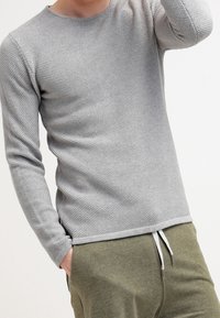 Lichtgrijze langemouwen shirt met een gestructureerd breipatroon, ronde halslijn en aansluitende mouwen, gecombineerd met olijfgroene joggingsbroek.