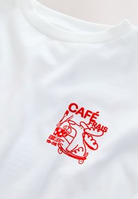 T-shirt en coton blanc avec un motif brodé rouge comprenant le texte « Café Frais » et des illustrations d'un personnage sur un skateboard.