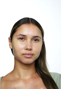 Närbild av en modells ansikte med klar hy, ljusa fräknar och rakt mörkt hår. Neutral bakgrund framhäver ansiktsdragen exklusivt.
