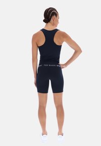 Tengerészkék aktív viselet készlet, amely egy testhezálló trikót tartalmaz versenyháttal, valamint hozzáillő, magas derekú rövidnadrágokat. A derékrészen a "TED BAKER" felirat olvasható.