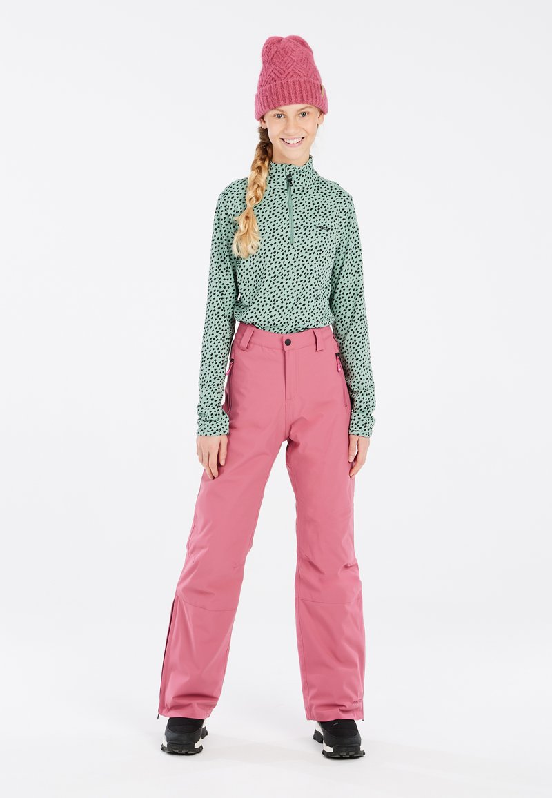 Maglia verde a maniche lunghe con pois neri, pantaloni da sci rosa e berretto rosa lavorato a maglia. Stivali neri con suola testurizzata.